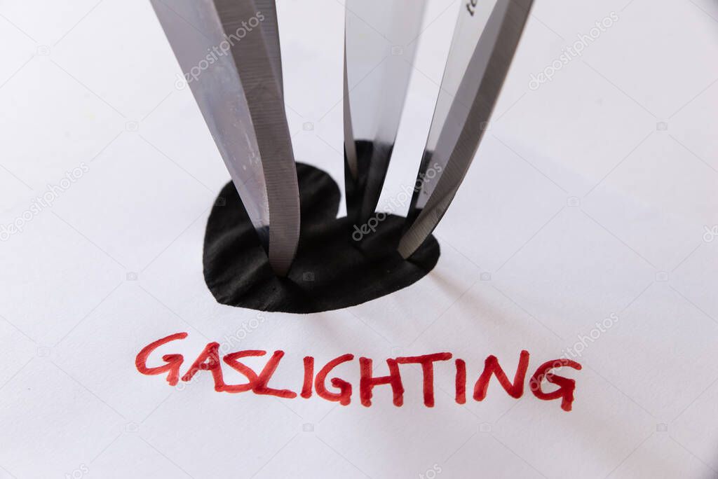Word Gaslighting, written in red on white paper, next to black heart design, with knife blades