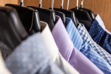 Çeşitli renklerde gömlekler, ahşap renkli bir gardıropta askılarda yan yana asılıydı.