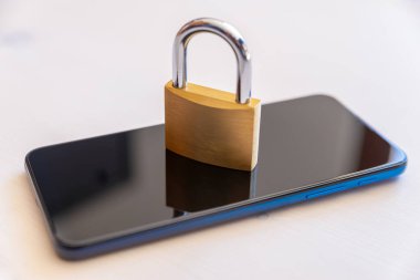 Üzerinde asma kilit olan beyaz bir yüzeye yerleştirilmiş akıllı telefon. Elektronik cihazların güvenliği ve ihlal edilemezliği ve bunların verilerinin korunması.
