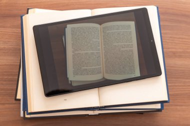 Üstünde tablet olan açık kitapları üst üste koyuyor. E-kitap ve e-okuyucu. Dijital biçimdeki kitaplar.