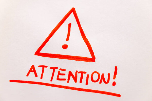Знак внимания, нарисованный красным маркером, и написанное "внимание", на белом листе, сфотографировано