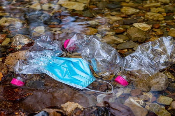 Masks and plastic bottles thrown into the waters of a stream.