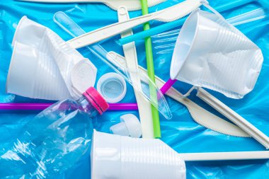 Mavi plastik yüzeyde tek kullanımlık plastik atıklar, bardaklar, bıçaklar, çatallar, şişeler. Plastiğin geri dönüşümü ve yeniden kullanımı. 