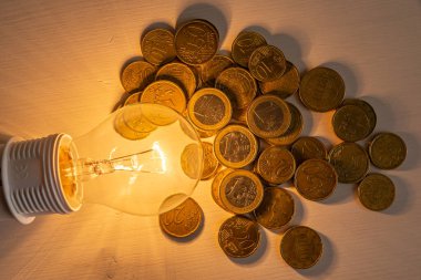Yanında bozuk paralar olan bir ampul. Enerji tarifelerini arttırın. Verimlilik ve enerji tasarrufu. 