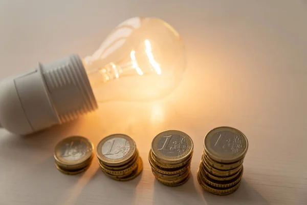 Lit light bulb with coins beside it. Increase in energy tariffs. Efficiency and energy saving.