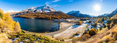 Sils Gölü 'nün panoramik manzarası, Maloja köyü ve çevresindeki dağlar, sonbaharda ve yeşilliklerle çevrelenmiş..