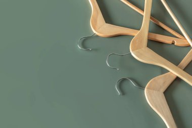 Boş ahşap elbise askıları koyu yeşil arka planda asılı ve fotokopi alanı var. Satış ve alışveriş konsepti.