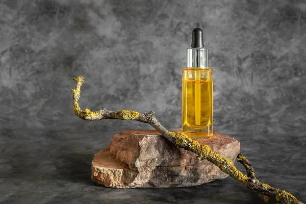 Glass bottle with cosmetic essential oil and natural stone stand on dark background. Organic natural product.