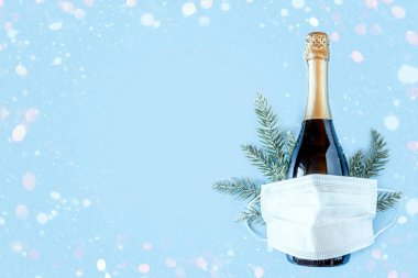 Şişe şampanya, ladin dalları ve mavi arka planda koruyucu tıbbi maske. Koronavirüs enfeksiyonu salgını sırasında Noel ve Yeni Yıl. Düz konum, üst görünüm, kopyalama alanı. Pankart