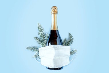 Şişe şampanya, ladin dalları ve mavi arka planda koruyucu tıbbi maske. Koronavirüs enfeksiyonu salgını sırasında Noel ve Yeni Yıl. Düz konum, üst görünüm, kopyalama alanı. Pankart