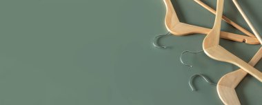 Boş ahşap elbise askıları koyu yeşil arka planda asılı ve fotokopi alanı var. Satış ve alışveriş konsepti.