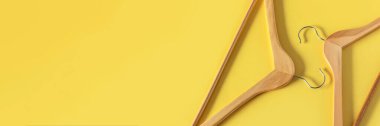 Boş ahşap elbise askıları sarı arka planda asılı ve fotokopi alanı var. Satış ve alışveriş konsepti.