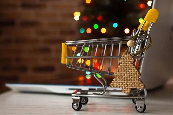 クリスマスオンラインショッピング 家でショッピングカートとノートパソコンぼやけたボケのライトとクリスマスツリーの背景に — ストック写真
