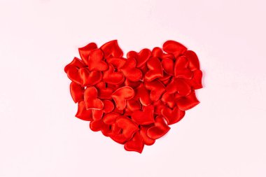 Sevgililer Günü, düğün, aşk konsepti. Pembe arka planda küçük kırmızı saten kalplerden yapılmış büyük bir kalp. Üst görünüm, düz görünüm, kopyalama alanı.