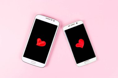 Siyah ekranlı cep telefonu ve pembe pastel arka planda izole edilmiş kırmızı kalp. Üst görünüm, düz görünüm, kopyalama alanı. Sevgililer günü, aşk, teknoloji, online flört konsepti..