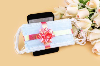 Gül buketi ve pastel arka planda siyah hediye kutusunda pembe fiyonklu koruyucu maskeler. Tatil hediyesi, doğum günü, Anneler Günü, Sevgililer Günü, Coronavirus salgını sırasında kadınlar günü..