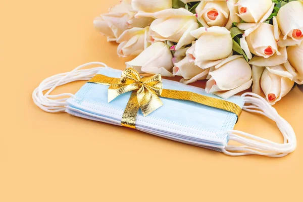 バラの花束と黄金のリボンとパステルの背景に弓を持つ保護医療用マスク コピースペース フラットレイアウト 誕生日 結婚式 母の日 パンデミックの間のバレンタインデーの贈り物 — ストック写真