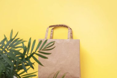 Tekrar kullanılabilir boş bir torba ve sarı arka planda yeşil dallı palmiye yaprakları. Sıfır atık, çevre dostu. Ağlı çanta. Düz konum, üst görünüm, kopyalama alanı