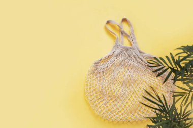 Tekrar kullanılabilir boş bir torba ve sarı arka planda yeşil dallı palmiye yaprakları. Sıfır atık, çevre dostu. Ağlı çanta. Düz konum, üst görünüm, kopyalama alanı