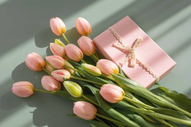 Pembe lale buketi ve yeşil arka planda gölgeli hediye kutusu. Bahar çiçekleri. Doğum günü, kadın, anneler günü, düğün, sevgililer günü için tebrik kartı. Düz yatıyordu. Boşluğu kopyala