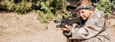 Çocuk optik görüşe bakıyor. Bir silah. Çocuklar dışarıda lazer savaşı oynuyorlar. Savaş simülasyon oyunu. Pankart