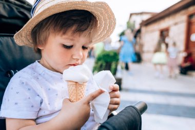 Saman şapkalı şirin bir çocuğun portresi bebek arabasında dondurma ile oturuyor. Şehrin arka planında gözleme külahında dondurma yiyen bir çocuk. Sütsüz dondurma..