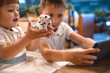 Çocuk ve bebek, restoranda siparişleri beklerken internetten tablette video oyunu oynuyorlar. Akıllı telefon kullanan çocuklar. Çocuklar teknolojiyi kullanıyor. Ekran zaman bağımlılığı.