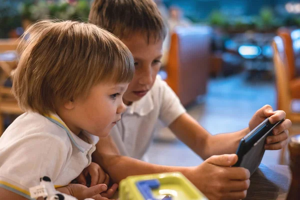 Çocuk ve bebek, restoranda siparişleri beklerken internetten tablette video oyunu oynuyorlar. Akıllı telefon kullanan çocuklar. Çocuklar teknolojiyi kullanıyor. Ekran zaman bağımlılığı.