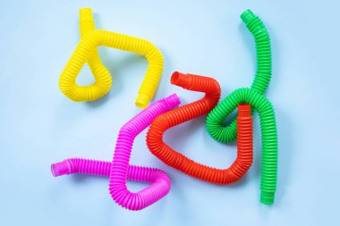 Renkli stres önleyici hareketler mavi arka plandaki çocuklar için pop tüpü duyusal oyuncakları itiyor. Üst manzara, düz yatış. Popüler plastik esnek kıvrımlı boruyla yaratıcı oyunun yakın plan çekimi.