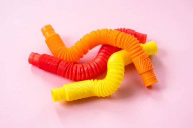 Renkli stres önleyici hareketler, pembe arka plandaki çocuklar için pop tüpü duyusal oyuncakları itiyor. Üst manzara, düz yatış. Popüler plastik esnek kıvrımlı boruyla yaratıcı oyunun yakın plan çekimi.
