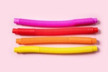 Renkli stres önleyici hareketler, pembe arka plandaki çocuklar için pop tüpü duyusal oyuncakları itiyor. Üst manzara, düz yatış. Popüler plastik esnek kıvrımlı boruyla yaratıcı oyunun yakın plan çekimi.
