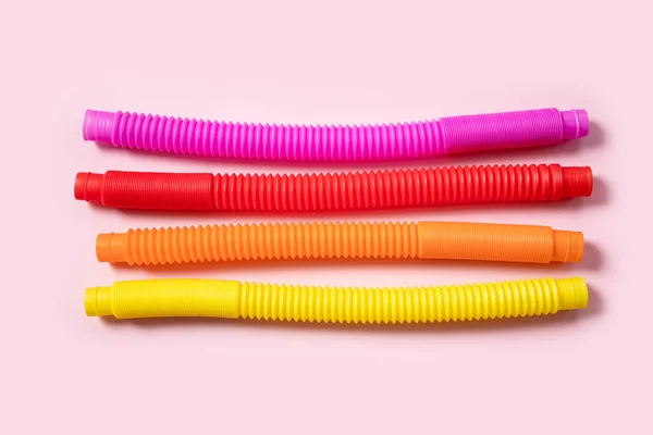Renkli stres önleyici hareketler, pembe arka plandaki çocuklar için pop tüpü duyusal oyuncakları itiyor. Üst manzara, düz yatış. Popüler plastik esnek kıvrımlı boruyla yaratıcı oyunun yakın plan çekimi.