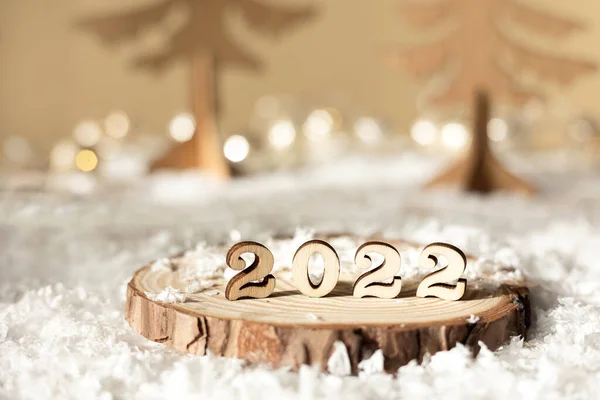 Yeni yıl 2022. 2022 numaralı ahşap tezgahta bej renkli pastel üzerinde dekoratif köknar ağaçları, kar ve ışıklar ile bulanık arka plan. Noel tebrik kartı..
