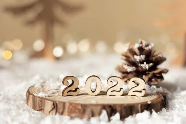 Yeni yıl 2022. 2022 numaralı ahşap tezgahta bej renkli pastel üzerinde dekoratif köknar ağaçları, koni, kar ve ışıklar ile bulanık arka plan. Noel tebrik kartı..