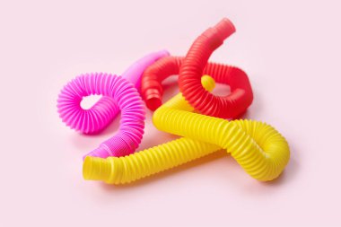 Renkli stres önleyici hareketler, pembe arka plandaki çocuklar için pop tüpü duyusal oyuncakları itiyor. Üst manzara, düz yatış. Popüler plastik esnek kıvrımlı boruyla yaratıcı oyunun yakın plan çekimi.