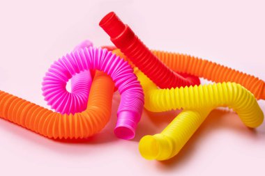 Renkli stres önleyici hareketler, pembe arka plandaki çocuklar için pop tüpü duyusal oyuncakları itiyor. Üst manzara, düz yatış. Popüler plastik esnek kıvrımlı boruyla yaratıcı oyunun yakın plan çekimi.