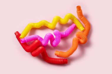 Renkli stres önleyici hareketler, pembe arka plandaki çocuklar için pop tüpü duyusal oyuncakları itiyor. Üst manzara, düz yatış. Popüler plastik esnek kıvrımlı boruyla yaratıcı oyunun yakın plan çekimi.