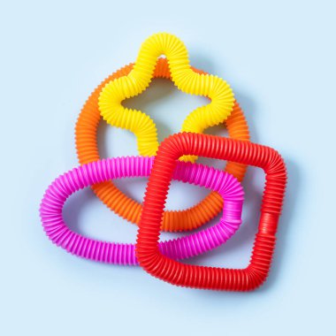 Renkli stres önleyici hareketler mavi arka plandaki çocuklar için pop tüpü duyusal oyuncakları itiyor. Üst manzara, düz yatış. Popüler plastik esnek kıvrımlı boruyla yaratıcı oyunun yakın plan çekimi.