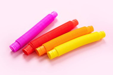 Renkli stres önleyici hareketler, pembe arka plandaki çocuklar için pop tüpü duyusal oyuncakları itiyor. Üst manzara, düz yatış. Popüler plastik esnek kıvrımlı boruyla yaratıcı oyunun yakın plan çekimi.