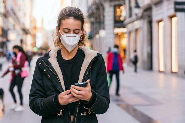 Yeni normal. Genç kız akıllı telefonunu kullanıyor. Genç kız akıllı telefonunu kullanıyor. Yeni teknolojiler. Akıllı telefonunuzu kullanıyorsunuz. Covid 'e karşı maske. Yüz maskeli bir genç. Salgın. Gençler konuşuyor..