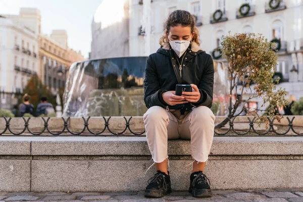 Yeni normal. Genç kız akıllı telefonunu kullanıyor. Genç kız akıllı telefonunu kullanıyor. Yeni teknolojiler. Akıllı telefonunuzu kullanıyorsunuz. Covid 'e karşı maske. Yüz maskeli bir genç. Salgın. Gençler konuşuyor..
