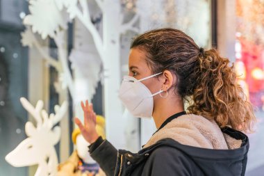 Yeni normal. Noel penceresine bakan bir genç. Noel tarzında dekore edilmiş bir mağazanın camına bakan genç bir kız. Çete. Maske takan bir genç. Yaşam biçimi