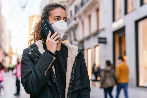 Yeni normal. Ergen, akıllı telefonuyla konuşuyor. Maskeli bir genç. Koruyucu maskeli genç kız. Salgın. Caddenin ortasında maskeli bir kız. Akıllı telefonuyla konuşan genç bir kız.
