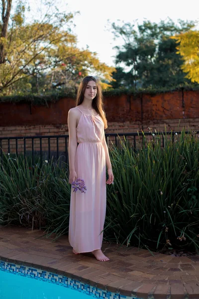 A young girl in a long dress stands near the pool. Bride in a pink dress. A graduate in a beautiful outfit.