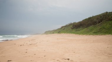 Hint Okyanusu 'nda bulutlu havada yeşil tepeleri olan güzel boş kumlu plaj. Yaz tatili. Tatilde. Güney Afrika. seçici odak