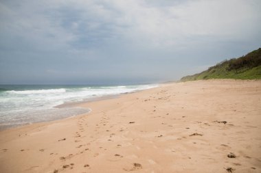 Hint Okyanusu 'nda bulutlu havada yeşil tepeleri olan güzel boş kumlu plaj. Yaz tatili. Tatilde. Güney Afrika. seçici odak