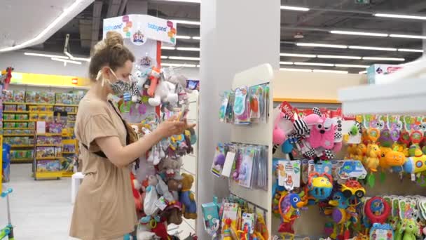 COVID-19 pandemic. Woman in protective mask shopping in childrens store. — Stock Video
