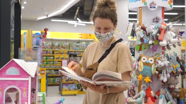Vrouw winkelen in beschermende masker kiest kinderen speelgoed. Tweede golf van coronavirus pandemie. 20 juli-2020. Warschau. Polen — Stockvideo