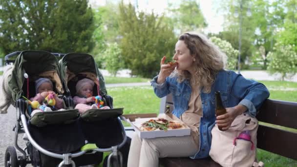 Mãe nova dos gêmeos do bebê que relaxam com pizza ao ar livre no parque — Vídeo de Stock