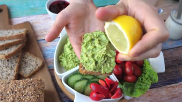 Сожмите лимон на тосте с авокадо в руке. — стоковое видео